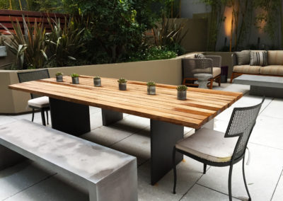 An outdoor modern patio with a large wooden table with six small potted succulent plants in tin containers.